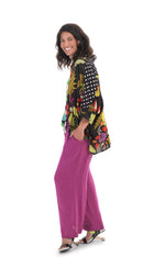 Load image into Gallery viewer, Left side full body view of the alembika floral mix print campshirt. This shirt  has a light colored jungle print on the right side and a dark colored jungle print on the left side. The shirt has a button down front, dotted sleeves, a relaxed fit, and drop shoulders. On the bottom she is wearing pink pants.
