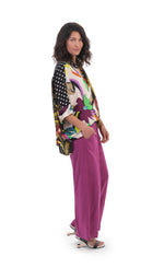 Load image into Gallery viewer, Right side full body view of the alembika floral mix print campshirt. This shirt has a light colored jungle print on the right side and a dark colored jungle print on the left side. The shirt has a button down front, dotted sleeves, a relaxed fit, and drop shoulders. On the bottom she is wearing pink pants.

