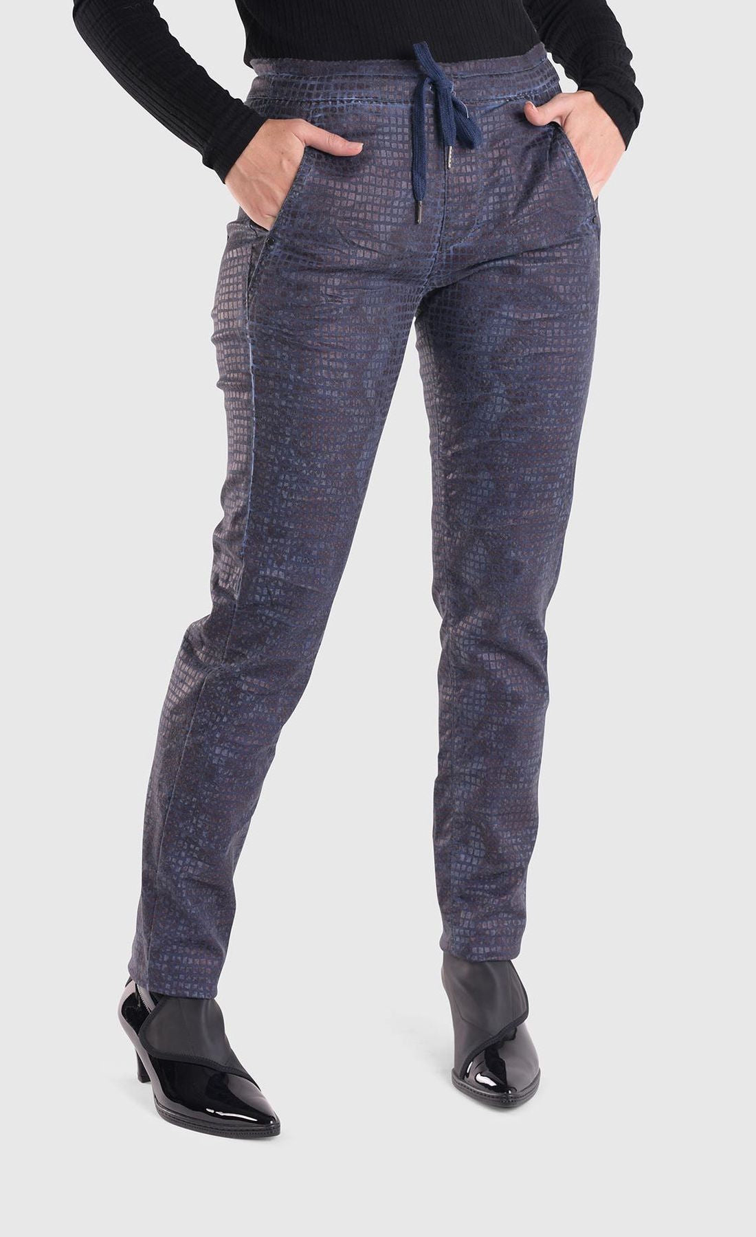Front bottom half view of a woman wearing the alembika iconic stretch jeans in indigo. These pull-on jeans have a drawstring waistband, a straight leg, and two front slant pockets.