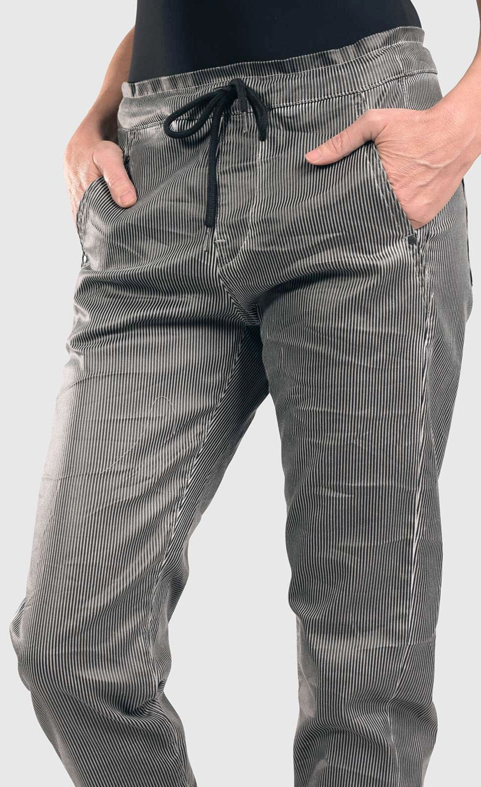 front bottom half close up view of a woman wearing the alembika iconic stretch jeans in a pinstripe black and white print. This pant has a drawstring waistband with a tie, two front pockets, and a relaxed slim leg.