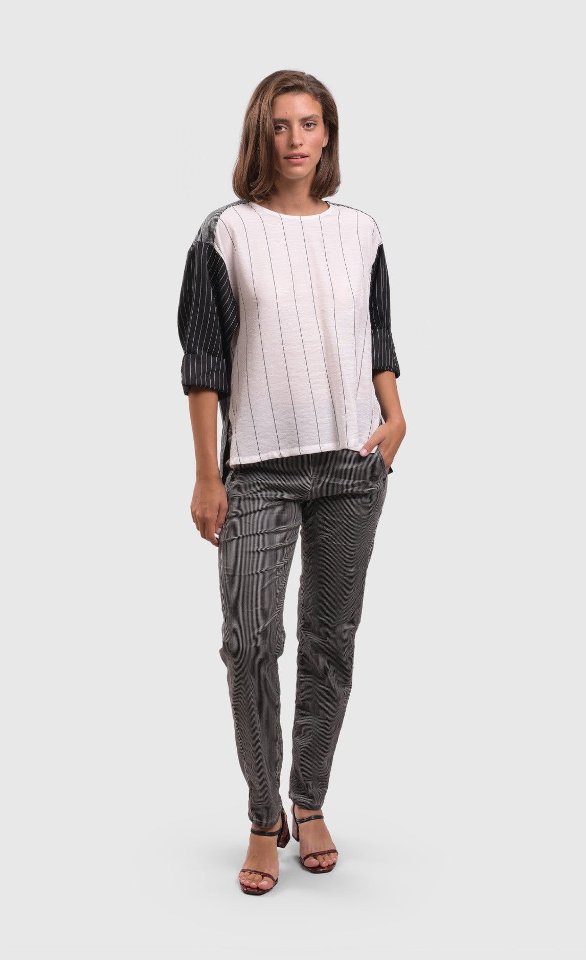 front full body view of a woman wearing a black and white top and the alembika iconic stretch jeans in a pinstripe black and white print. This pant has a drawstring waistband with a tie, two front pockets, and a relaxed slim leg.