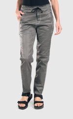 Load image into Gallery viewer, front bottom half view of a woman wearing the alembika iconic stretch jeans in a pinstripe black and white print. This pant has a drawstring waistband with a tie, two front pockets, and a relaxed slim leg.
