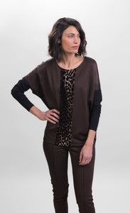 Front top half view of a woman wearing brown pants and the alembika leopard panel top. This top has a round neck, solid black drop shoulder dolman sleeves, a brown body, and a leopard print panel running down the center of the front.
