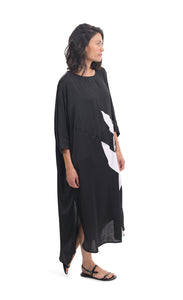 Right side full body view of a woman wearing the alembika lotus caftan dress in black. This dress sits below the knees. It has 3/4 length sleeves, side slits, and a large white lotus flower on the front.