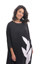 Load image into Gallery viewer, Front top half view of a woman wearing the alembika lotus caftan dress in black. This dress sits below the knees. It has 3/4 length sleeves, side slits, and a large white lotus flower on the front.
