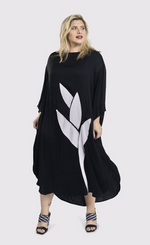 Load image into Gallery viewer, Front full body view of a woman wearing the alembika lotus caftan dress in black. This dress sits below the knees. It has 3/4 length sleeves, side slits, and a large white lotus flower on the front.
