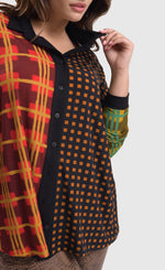 Load image into Gallery viewer, Front top half close up view of a woman wearing brown pants and the alembika multi check blouse. This blouse has a mix of plaid and checkered prints on the front, a button up front, and dolman long sleeves..
