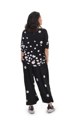 Load image into Gallery viewer, Back, full body view of a woman wearing the alembika multi spotted lia jersey top. This top is black with different types of white spots all over it. The sleeves are 3/4 length and the shirt has an oversized fit. On the bottom she is wearing full leg black pants with white dots.
