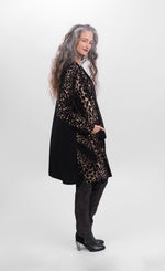Load image into Gallery viewer, RIght side full body view of a woman wearing the alembika nala velvet jacket in leopard print. This jacket has long sleeves, two front pockets, and a draped open front. The jacket sits below the hips. The back is solid black
