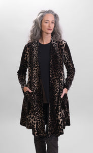 Front top half view of a woman wearing the alembika nala velvet jacket in leopard print. This jacket has long sleeves, two pockets, and a draped open front. The jacket sits below the hips.
