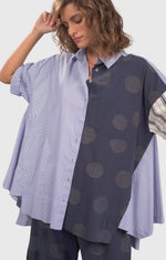 Load image into Gallery viewer, Front top half view of a woman wearing blue pants with green dots and the alembika navy short sleeve shirt. This shirt has blue and white stripes on the front right side and blue with green dots on the left side.
