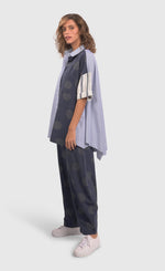 Load image into Gallery viewer, Front left full body view of a woman wearing blue pants with green dots and the alembika navy short sleeve shirt. This shirt has blue and white stripes on the front right side and back and blue with green dots on the left side.
