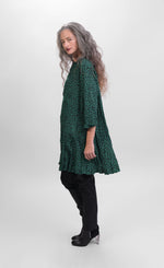 Load image into Gallery viewer, Left side full body view of a woman wearing the alembika pine spot top. This top is green with black cheetah print. The top has a 3/4 button down front and long sleeves.
