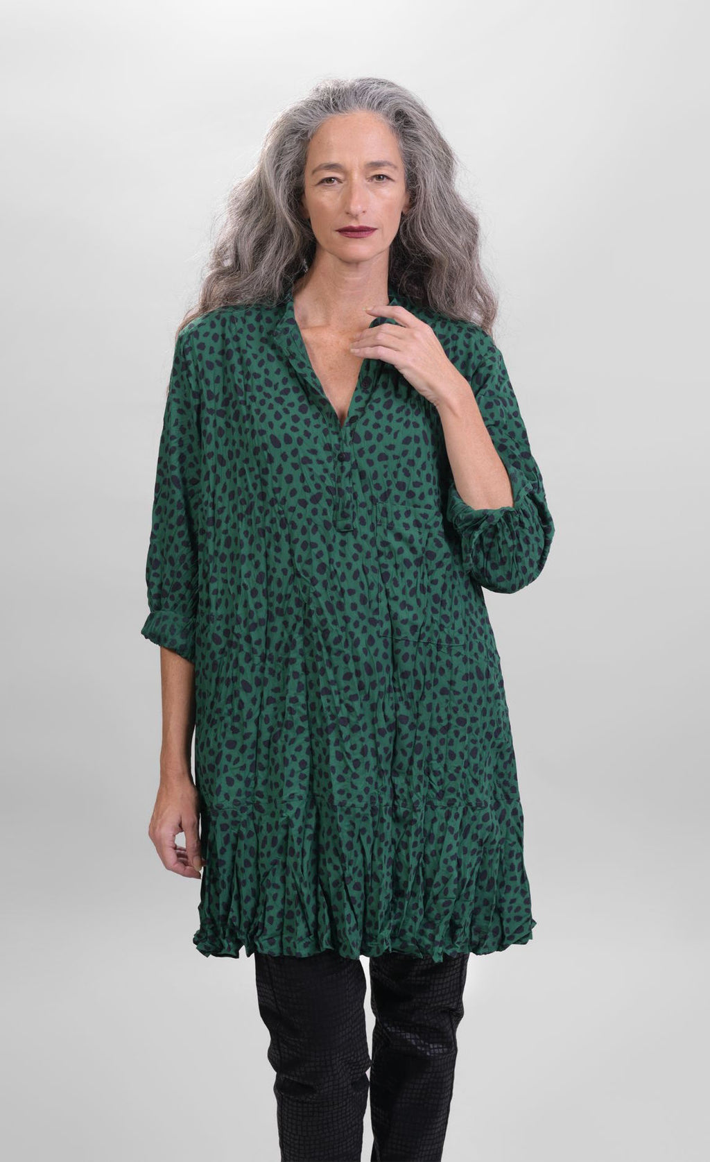 Front top half view of a woman wearing the alembika pine spot top. This top is green with black cheetah print. The top has a 3/4 button down front and long sleeves.