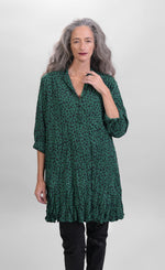Load image into Gallery viewer, Front top half view of a woman wearing the alembika pine spot top. This top is green with black cheetah print. The top has a 3/4 button down front and long sleeves.
