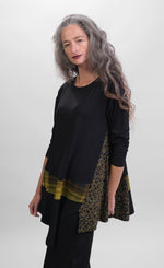 Load image into Gallery viewer, Front top half view of a woman wearing black pants and the alembika plaid asymmetry top. This top is black with a cheetah print side panel on the left side, long sleeves, and a horizontal green and yellow plaid panel running across the bottom of the top. The from hem is asymmetrical.
