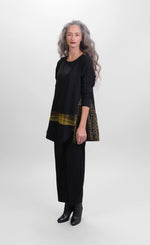 Load image into Gallery viewer, Front full body view of a woman wearing black pants and the alembika plaid asymmetry top. This top is black with a cheetah print side panel on the left side, long sleeves, and a horizontal green and yellow plaid panel running across the bottom of the top. The from hem is asymmetrical.

