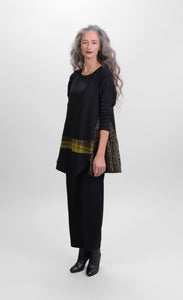 Front full body view of a woman wearing black pants and the alembika plaid asymmetry top. This top is black with a cheetah print side panel on the left side, long sleeves, and a horizontal green and yellow plaid panel running across the bottom of the top. The from hem is asymmetrical.