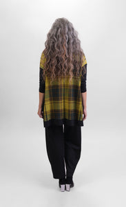 Back view of a woman wearing black pants and the alembika plaid trapeze top. This top is a yellow and green plaid with solid black drop shoulder long sleeves. The top has black detailing around the hem