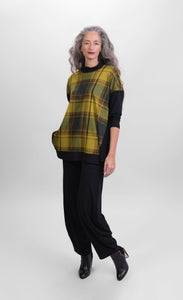 Front full body view of a woman wearing black pants and the alembika plaid trapeze top. This top is a yellow and green plaid with solid black drop shoulder sleeves. The top has a funnel neck, side slits, and black detailing around the hem
