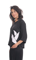Load image into Gallery viewer, Left side top half view of a woman wearing black pants and the alembika lotus top in black. This top has a round neck, 3/4 length sleeves, and a white lotus flower on the front left side.
