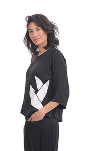 Left side top half view of a woman wearing black pants and the alembika lotus top in black. This top has a round neck, 3/4 length sleeves, and a white lotus flower on the front left side.