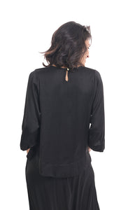 Back top half view of a woman wearing black pants and the alembika lotus top in black. This top a keyhole back and 3/4 length sleeves.