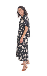 Load image into Gallery viewer, Left side full body view of a woman wearing the alembika mandala wide pant and the alembika speckle mandala shirt. This shirt has a black and white mandala tie dye print, a button down front, a shirt collar, a boxy silhouette, and short sleeves. The wide pants have the same print as the top.
