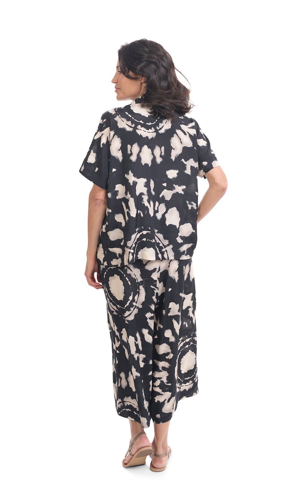Back full body view of a woman wearing the alembika mandala wide pant and the alembika speckle mandala shirt. This shirt has a black and white mandala tie dye print, a boxy silhouette, and short sleeves. The wide pants have the same print as the top.