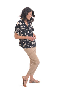 Front full body view of a woman wearing khaki pants and the alembika speckle mandala shirt. This shirt has a black and white mandala tie dye print, a button down front, a shirt collar, a boxy silhouette, and short sleeves.