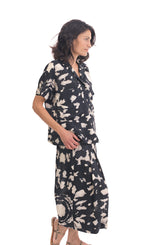 Load image into Gallery viewer, Right side full body view of a woman wearing the alembika mandala wide pant and the alembika speckle mandala shirt. This shirt has a black and white mandala tie dye print, a button down front, a shirt collar, a boxy silhouette, and short sleeves. The wide pants have the same print as the top.
