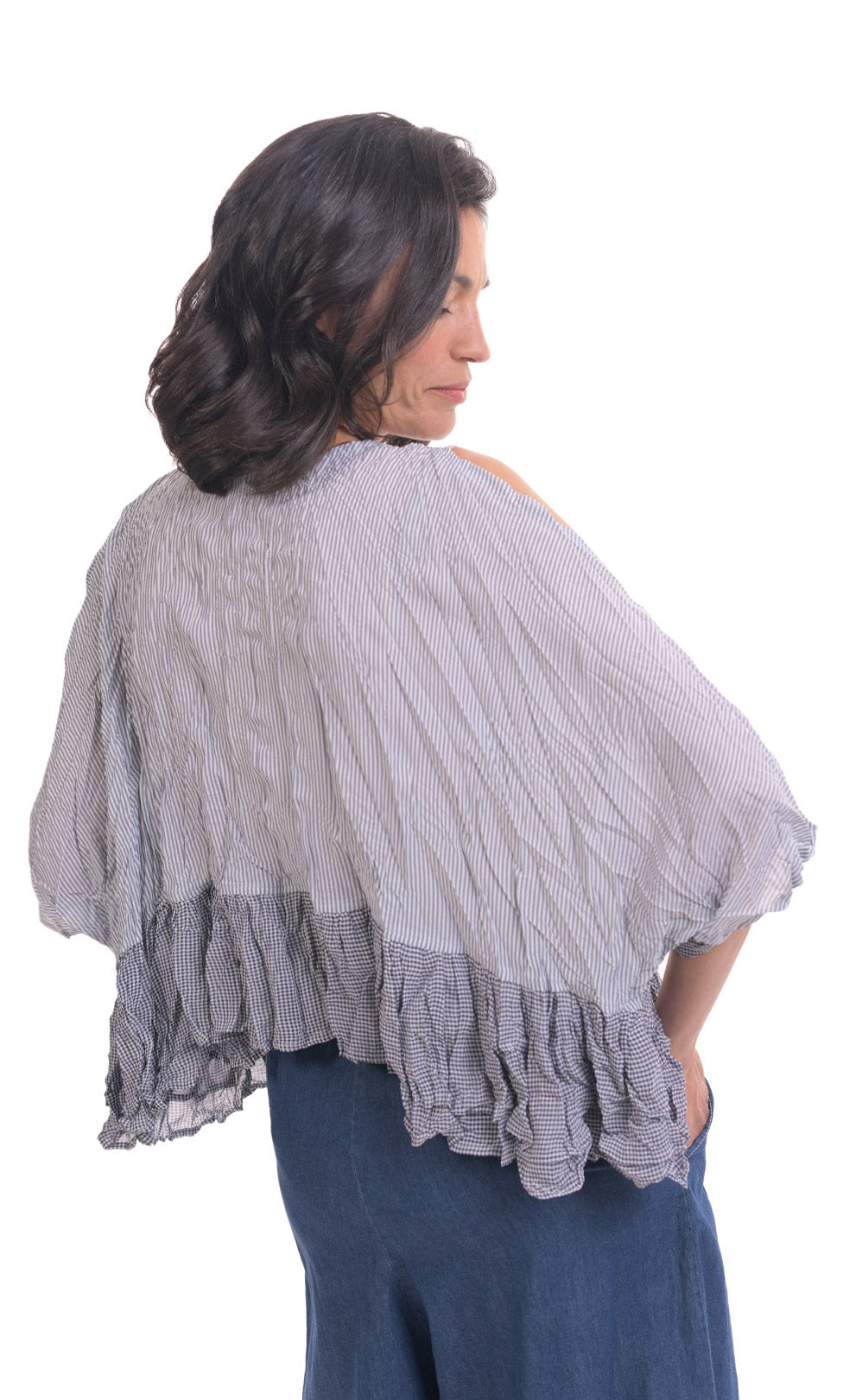 Back top half view of a woman wearing wide jeans and the alembika gingham Rhys Ruffled Blouse. This top has a blue and white plaid print, cold shoulder 3/4 length sleeves, and a ruffled hem.