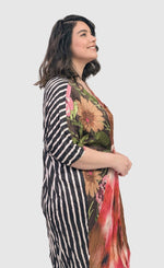 Load image into Gallery viewer, Front right side full top half view of a woman wearing the alembika skye caftan butterfly dress. This dress has pink flowers over a brown backdrop on the right side, a pink and brown tie dye print in the center, and a black and white striped print on the back.
