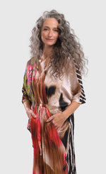 Load image into Gallery viewer, Front left side top half view of a woman wearing the alembika skye caftan butterfly dress. This dress has pink flowers over a brown backdrop on the right side, a pink and brown tie dye print in the center, a beige and brown tie dye print on the left side, and a black and white striped print on the back.
