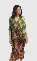 Load image into Gallery viewer, Front full body view of a woman wearing the alembika skye caftan dress in the color aquamarine. This dress has green, yellow, and blue tie dye on the left side, blue and green stripes on the right side and back, and pink flowers on a brown backdrop down the center of the front. The center of the front of the dress is tied to bring the waist in.
