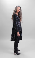 Load image into Gallery viewer, Right side full body view of a woman wearing black pants and the alembika smoke echo asymmetric tunic. This tunic is black, blue, and grey tie-dye with black spots all over it. The top has a round neck, long sleeves, and an asymmetrical hi-lo hem.
