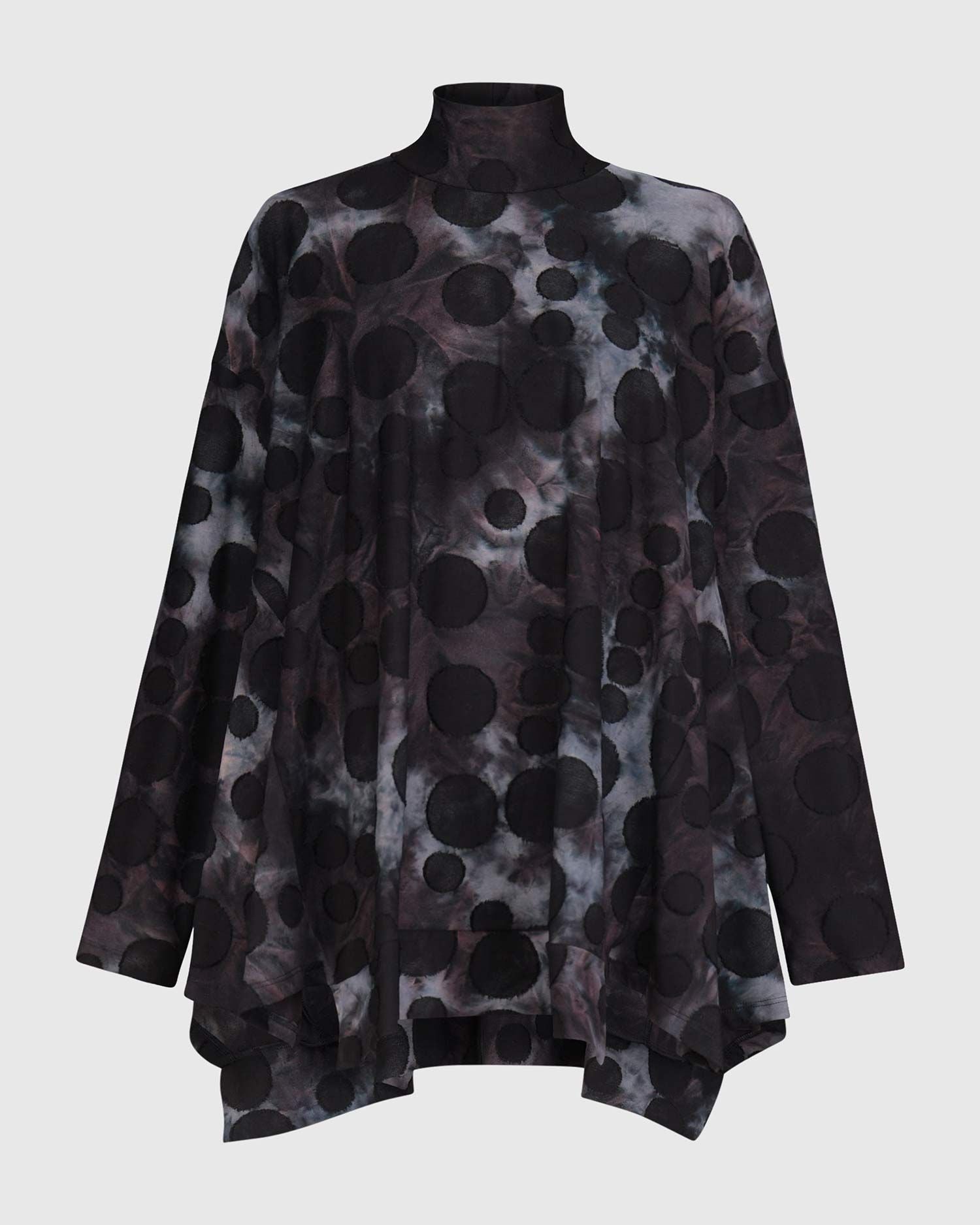Front view of the alembika swing top in smoke. This top is black, grey, and blue tie dye with black dots all over it. The top has a mock neck, long sleeves, and a wide flowy silhouette with a stepped hem.
