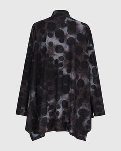 Back view of the alembika swing top in smoke. This top is black, grey, and blue tie dye with black dots all over it. The top has a mock neck, long sleeves, and a wide flowy silhouette with a stepped hem.