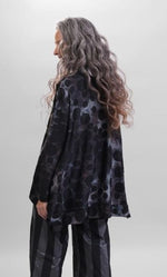 Load image into Gallery viewer, Back top half view of a woman wearing the alembika swing top in smoke. This top is black, grey, and blue tie dye with black dots all over it. The top has a mock neck, long sleeves, and a wide flowy silhouette with a stepped hem.
