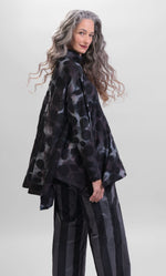 Load image into Gallery viewer, Back top half view of a woman wearing the alembika swing top in smoke. This top is black, grey, and blue tie dye with black dots all over it. The top has a mock neck, long sleeves, and a wide flowy silhouette with a stepped hem.
