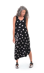 Front full body view of a woman wearing the alembika Lia Spotted Jersey Hi-Low Maxi Dress. This sleeveless dress is black with white spiral circles all over it. The front has a scoop neck and a front, right-sided draped pocket. The hem is asymmetrical.