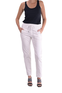 Front full body view of a woman wearing the alembika stretch denim pant. This pant is white with two front slant pockets and a drawstring waistband. The pants have a relaxed skinny silhouette.