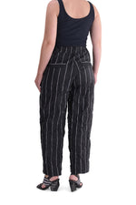 Load image into Gallery viewer, Back bottom half view of a woman wearing the alembika pinstriped pant. The pant is black with white pinstripes. The back has two welt pockets.  The waist is elastic and the pant sits right at the ankles. This pant has a straight leg silhouette.
