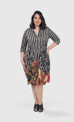 Load image into Gallery viewer, Front full body view of a woman wearing the alembika sunset wonderful dress. This dress has a button down front black and white striped print and a floral printed bottom. The dress has 3/4 length sleeves and a front draped pocket
