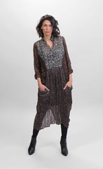 Load image into Gallery viewer, Front full body view of a woman wearing the alembika talia cocoon russet dress. This dress is slightly sheer with a slip. It has a mix of prints on it that are brown and black and white. The dress has a half button front and two draped pockets.
