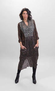 Front full body view of a woman wearing the alembika talia cocoon russet dress. This dress is slightly sheer with a slip. It has a mix of prints on it that are brown and black and white. The dress has a half button front and two draped pockets.