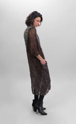 Load image into Gallery viewer, Right side full body view of a woman wearing the alembika talia cocoon russet dress. This dress is slightly sheer with a slip. It has a mix of prints on it that are brown and black and white. The dress has a front draped pocket that can be seen from the right side.
