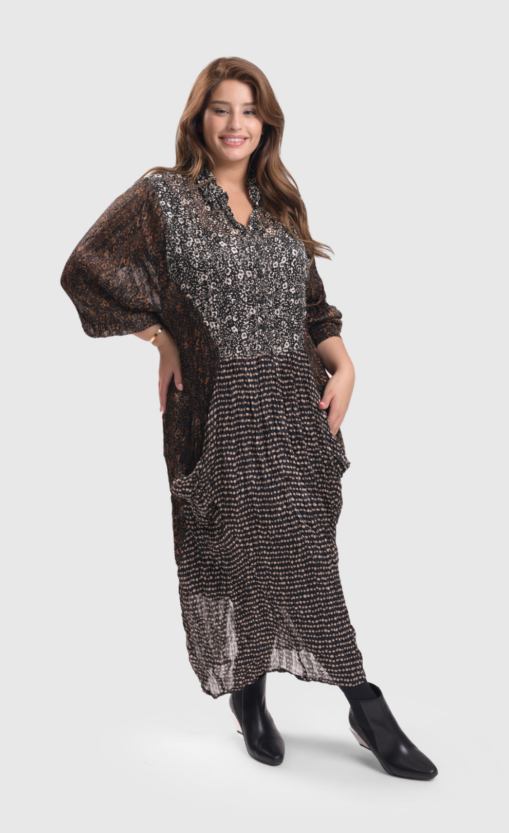 Front full body view of a woman wearing the alembika talia cocoon russet dress. This dress is slightly sheer with a slip. It has a mix of prints on it that are brown and black and white. The dress has a half button front and two draped pockets.