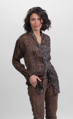 Load image into Gallery viewer, Front top half view of a woman wearing brown alembika pants and the alembika talia russet blouse. This long sleeved blouse has a button down front, a stand collar, and a mix of different prints that are brown, black, and white.
