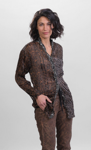 Front top half view of a woman wearing brown alembika pants and the alembika talia russet blouse. This long sleeved blouse has a button down front, a stand collar, and a mix of different prints that are brown, black, and white.